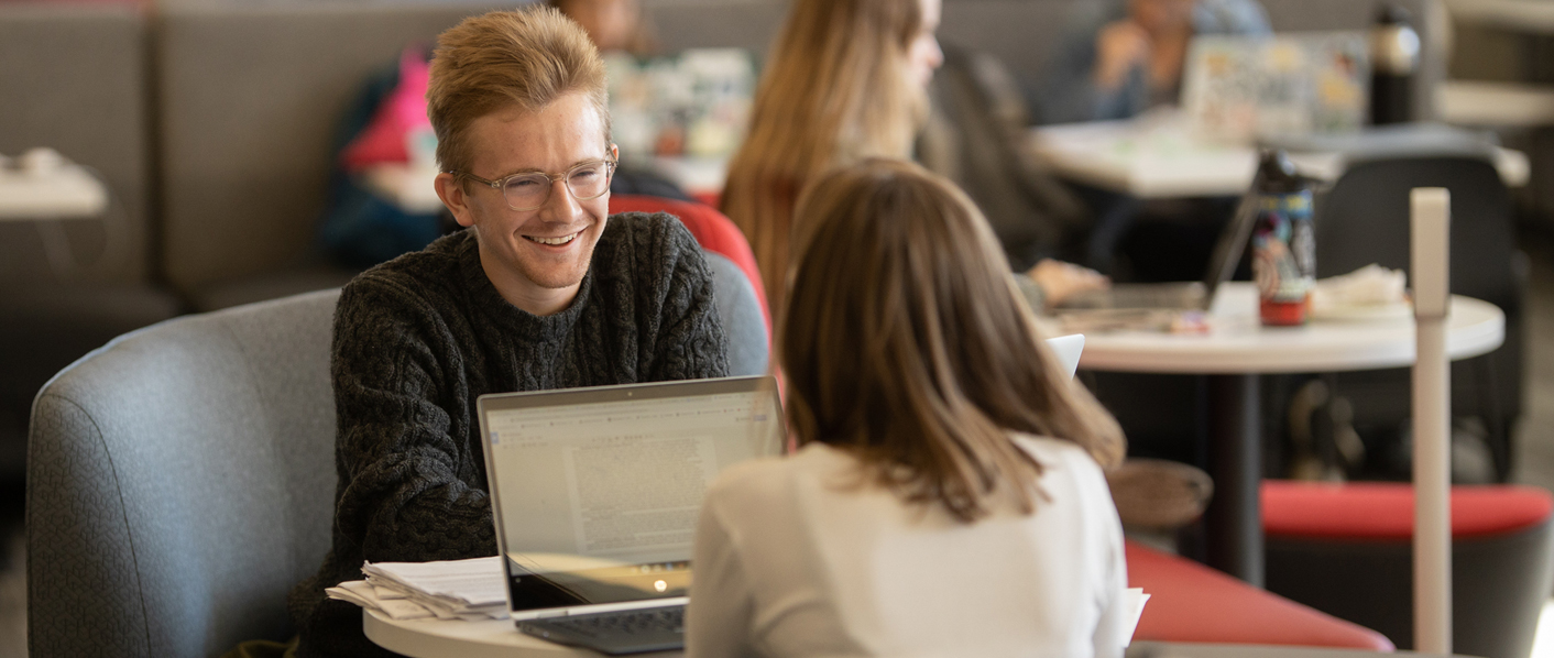 Two students talking with a laptop open